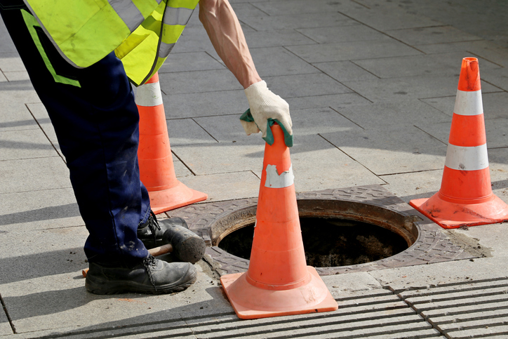 worker places traffic cones around hatch for sewer pipe repair